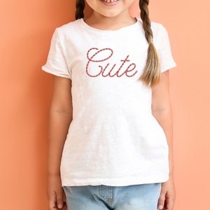 K&ouml;nnte beinhalten: Ein wei&szlig;es T-Shirt mit einem roten seilartigen Design, das das Wort "Cute" buchstabiert.