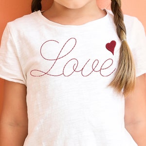 May include: White t-shirt with red embroidered lettering that says "Love" and a small red heart.