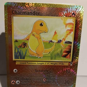 May include: A holographic Charmander Pokémon card. The card features an orange lizard-like creature with a flame on its tail. The card text includes "Charmander", "Scratch", and "Ember". The card is 2' 0" long and weighs 19 lbs.