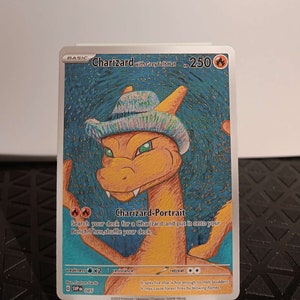 May include: A Charizard Pokemon trading card with a blue and white hat. The card is a basic card with a fire type and has a retreat cost of two colorless energy. The card text reads "Search your deck for a Charizard and put it onto your Bench. Then, shuffle your deck."