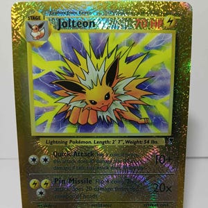May include: A holographic gold Jolteon Pokémon card. The card features a yellow and white electric-type Pokémon with a lightning bolt design. The card text includes "Quick Attack" and "Pin Missile" attacks. The card measures 2' 7" in length and weighs 54 lbs.