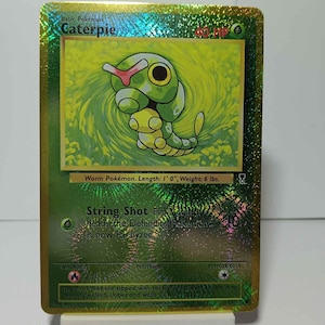 May include: A holographic Caterpie Pokémon trading card. The card features a green caterpillar with a red marking on its head. The text on the card includes "Caterpie", "String Shot", and "Worm Pokémon. Length: 1' 0", Weight: 6 lbs."