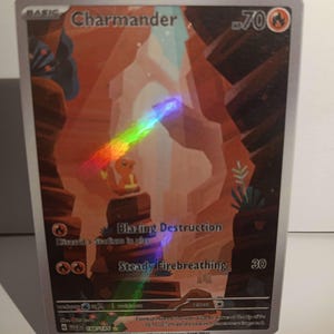 May include: A Pokemon trading card featuring Charmander, a fire-type Pokemon. The card is a basic card with a HP of 70. The card has two attacks: "Blazing Destruction" and "Steady Firebreathing".