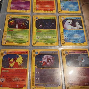 May include: Nine Pokémon trading cards in a binder. The cards have yellow borders and feature various Pokémon characters with different HP levels and attack descriptions. The cards are in a protective sleeve.