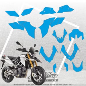 Könnte beinhalten: Ein weiß-schwarzes Aprilia-Motorrad mit goldenen Gabeln wird zusammen mit einer Reihe hellblauer Aufkleber gezeigt. Die Aufkleber sind in verschiedenen Formen und Größen, wahrscheinlich zur Individualisierung. Der Text "Stickers" ist enthalten.