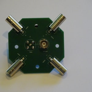 May include: A green circuit board with four BNC connectors and a center SMA connector. The board has labels for "radial", "feed", "vertical", and "radial".