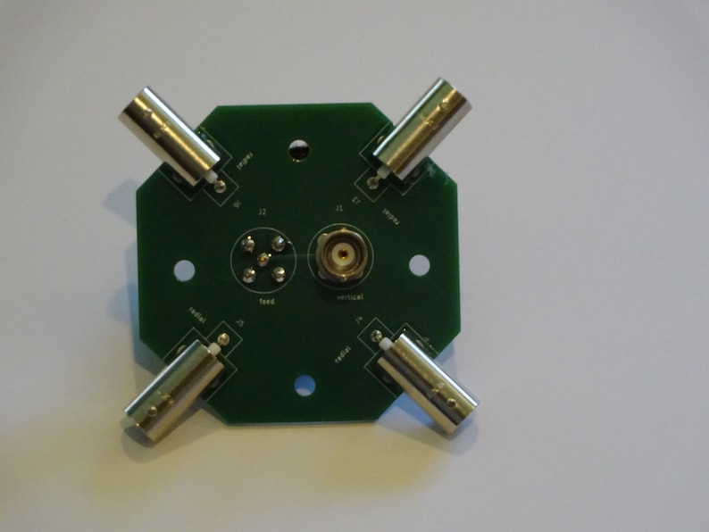 May include: A green circuit board with four BNC connectors and a center SMA connector. The board has labels for "radial", "feed", "vertical", and "radial".