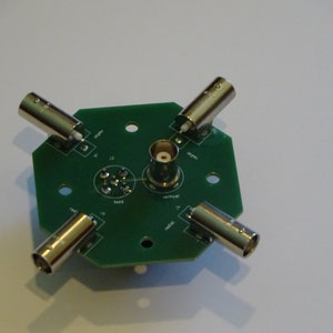 May include: A green circuit board with five BNC connectors and a central female BNC connector. The board is labeled with the words "feed", "vertical", "rotate", "type", and "12".