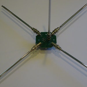 May include: A five-element antenna with a green circuit board base and silver metal rods. The antenna is designed for use with radio frequency signals.