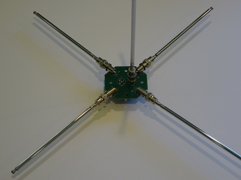 May include: A five-element antenna with a green circuit board base and silver metal rods. The antenna is designed for use with radio frequency signals.