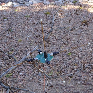 May include: A green circuit board with five copper antennas attached to it. The antennas are connected to the board with black connectors. The board is mounted on a branch of a tree.