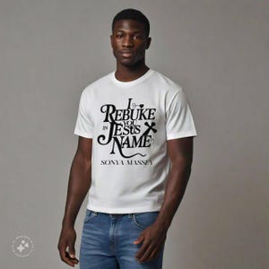 May include: White t-shirt featuring the text "I Rebuke You in Jesus Name" in black, decorative lettering. The name "Sonya Massey" is printed below. The shirt is paired with blue denim jeans.