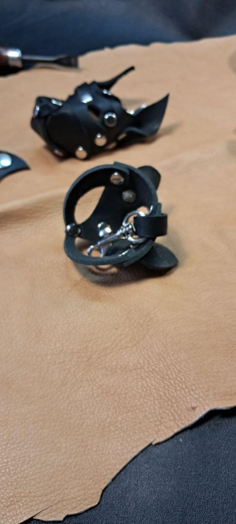 May include: Two black leather circular accessories featuring silver-toned metal rivets and a central silver-toned metal swivel clasp. The leather pieces are constructed with cut-out sections and secured with metal hardware, showcasing a structured design.