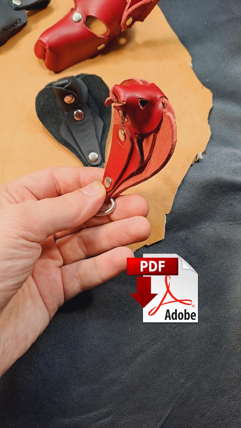 May include: A red leather keyring shaped like a bird, featuring silver-toned metal rivets and a circular metal ring. The keyring is constructed from layered leather pieces, showcasing a smooth finish and visible stitching details.