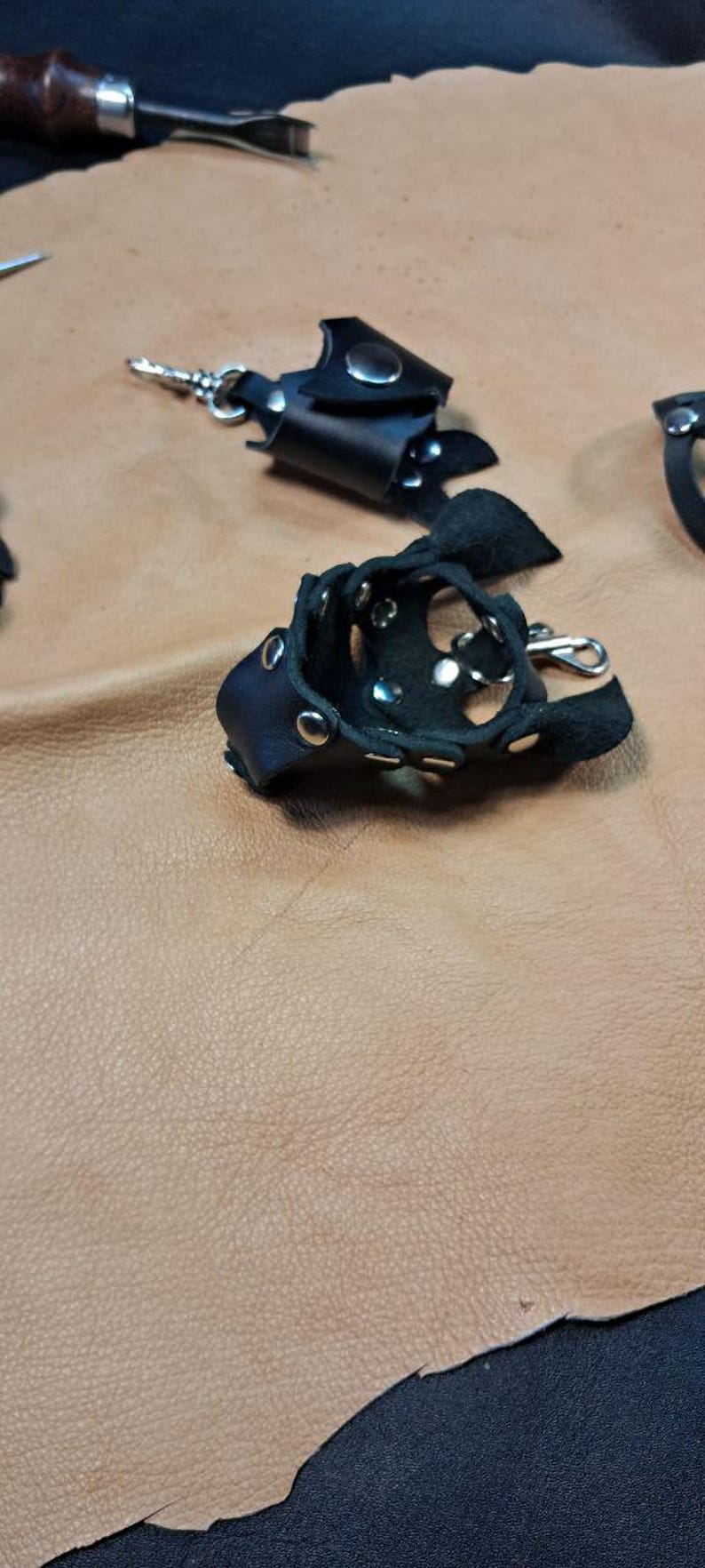 May include: Two black leather finger guards featuring silver-toned metal rivets and snap closures. Each guard has a small metal swivel clasp attached to the side, designed for securing the leather piece around a finger with adjustable metal hardware.