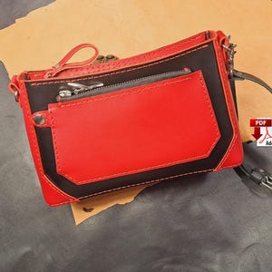 May include: A small black and red leather crossbody bag with a zipped pocket. The bag has a long strap and a short handle.