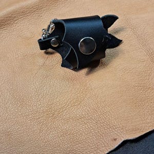 May include: Three black leather accessories featuring silver-toned metal snaps and hardware. Each piece is constructed from layered black leather segments, secured with circular metal rivets, and includes a small metal clip attachment.