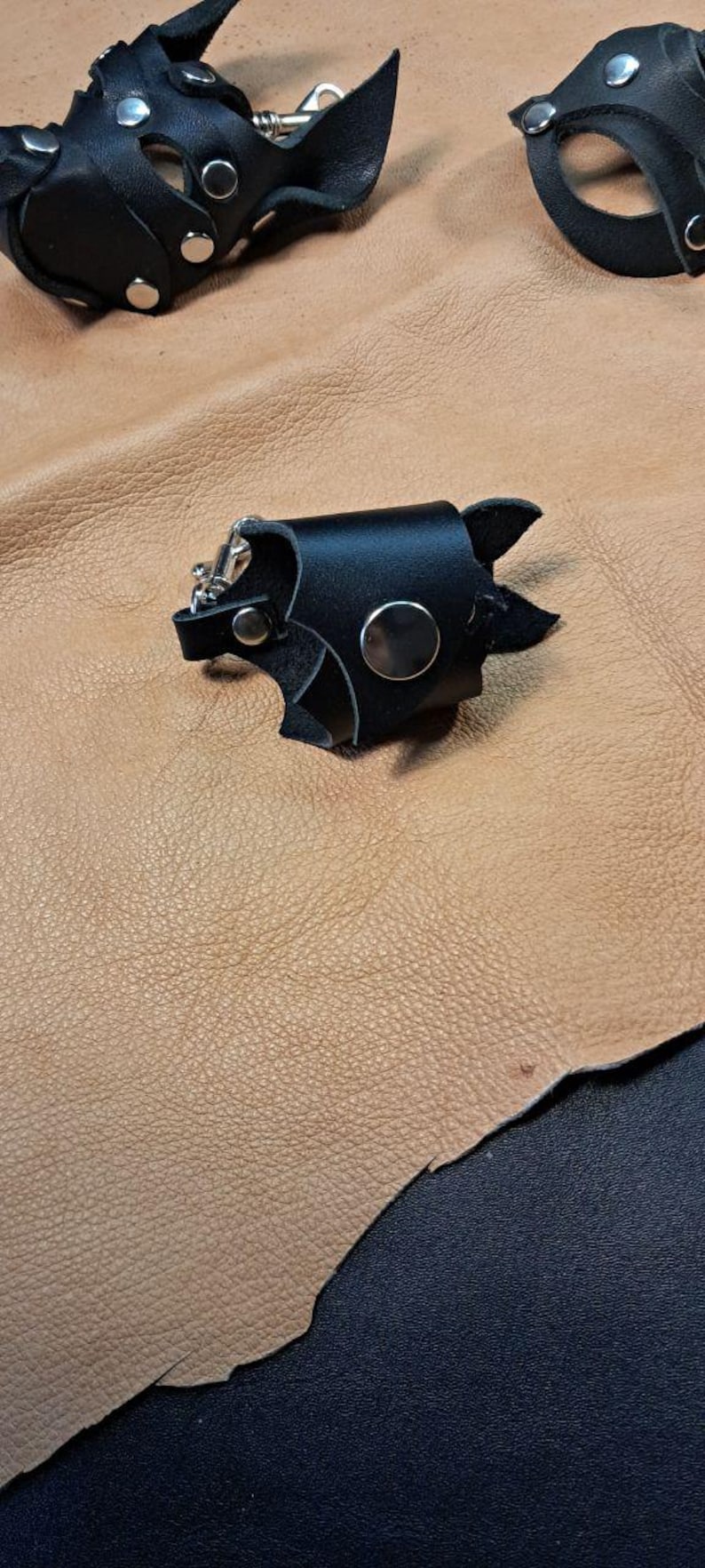 May include: Three black leather accessories featuring silver-toned metal snaps and hardware. Each piece is constructed from layered black leather segments, secured with circular metal rivets, and includes a small metal clip attachment.