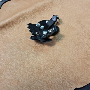May include: A black leather animal-shaped mask accessory featuring silver-toned metal rivets and a small metal clasp. The item is constructed from multiple layered leather pieces secured with studs, showcasing a distinct snout-like structure.