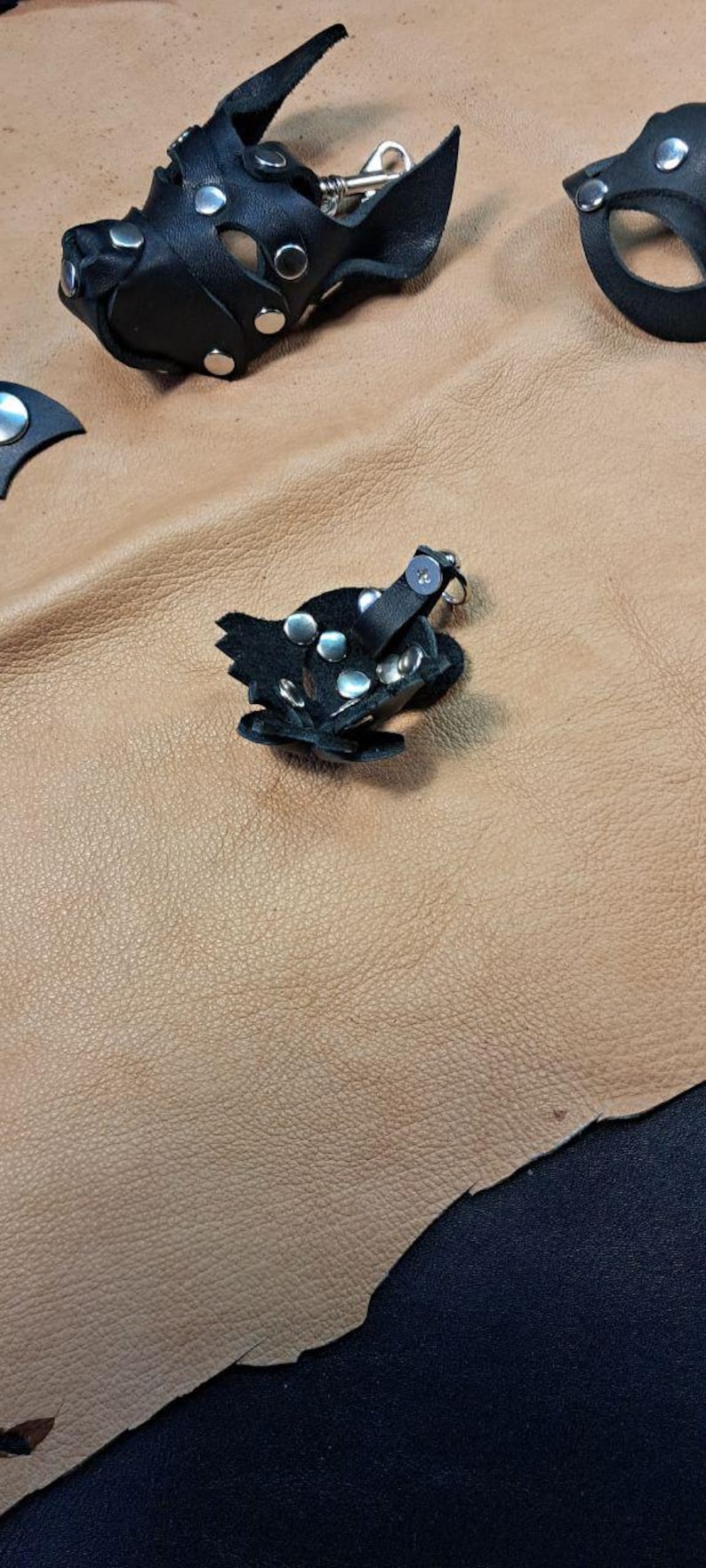 May include: A black leather animal-shaped mask accessory featuring silver-toned metal rivets and a small metal clasp. The item is constructed from multiple layered leather pieces secured with studs, showcasing a distinct snout-like structure.