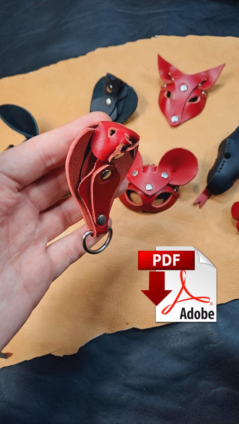 May include: A red leather cobra keyring with silver-tone metal rivets and a circular ring. Other leather animal-shaped items in red and black are visible in the background, including a fox mask and a mouse mask. A PDF Adobe icon is present.