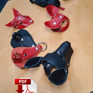 May include: A collection of red and black leather animal-shaped masks and accessories featuring silver-tone metal rivets and D-rings. The items are arranged on a tan leather hide. An Adobe PDF icon is visible in the lower left corner.