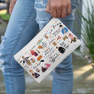 Könnte beinhalten: Weiße, rechteckige Kosmetiktasche mit schwarzem Reißverschluss, mit bunten Cartoon-Illustrationen und Text aus der Fernsehserie "Friends". Die Tasche enthält Sätze wie "I'm Fine" und "Could I BE wearing anymore clothes?"