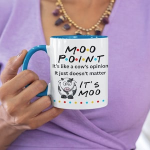 Peut inclure: Une tasse en céramique blanche avec un bord et une poignée bleus. La tasse présente une vache de dessin animé et le texte "MOO POINT It's like a cow's opinion it just doesn't matter IT'S MOO".