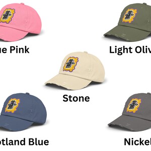 K&ouml;nnte beinhalten: F&uuml;nf Baseballkappen in verschiedenen Farben mit einem gestickten gelben und violetten Aufn&auml;her, auf dem in schwarzer Schrift "Ich bin f&uuml;r dich da" steht. Die Kappen sind in den Farben True Pink, Light Olive, Stone, Scotland Blue und Nickel erh&auml;ltlich.