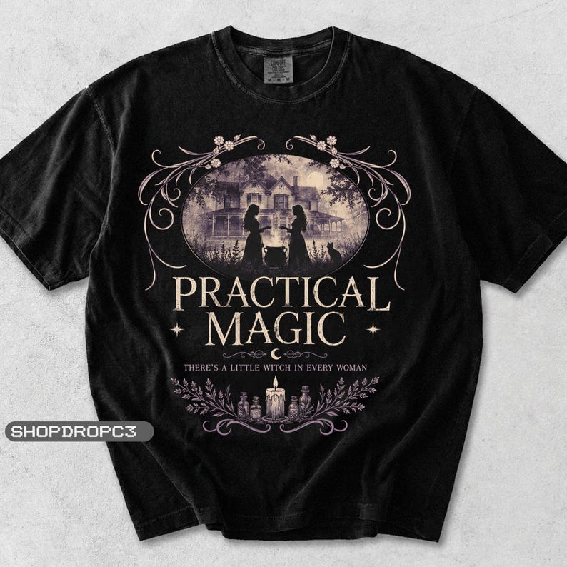 May include: A black t-shirt featuring a graphic print of a house, two figures, and a cauldron. The text reads PRACTICAL MAGIC and THERE'S A LITTLE WITCH IN EVERY WOMAN, accompanied by illustrations of a candle, bottles, and decorative floral vines.