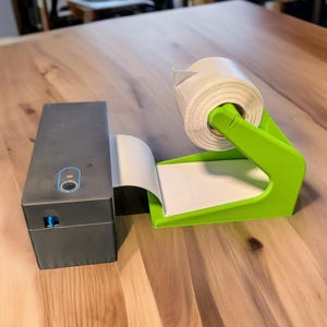 May include: A black label printer with a roll of white labels on a green label dispenser. The label dispenser has a white label roll and a green base.