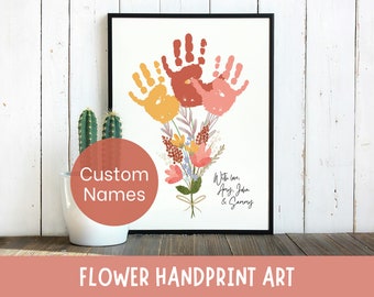 Puede incluir: Impresión artística enmarcada con un ramo de huellas de manos en tonos naranja y rosa, complementado con detalles florales. El texto dice "With love, Amy, John & Sammy". Las palabras "Custom Names" y "FLOWER HANDPRINT ART" también son visibles.