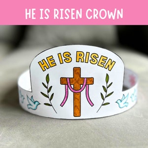 May include: A white paper crown with the words "He is Risen" in yellow letters. The crown also features a brown cross with pink ribbons, green leaves, and white doves.