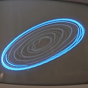 May include: A vintage television screen displays a glowing blue and white abstract design. The design is a series of concentric, oval-shaped lines, creating a mesmerizing visual effect. The screen is set within a gray frame.