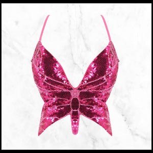 May include: A pink sequined butterfly-shaped crop top. The top has a V-neckline and adjustable straps.