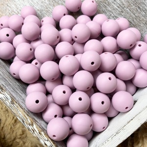 May include: A large bowl filled with a variety of light purple silicone beads. The beads are smooth and round, and they are perfect for making jewelry or other crafts.