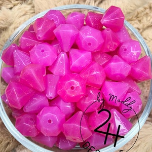 May include: A bowl of magenta glitter diamond-shaped beads. The beads are translucent and have a sparkly finish. The bowl is clear glass and has a white background.