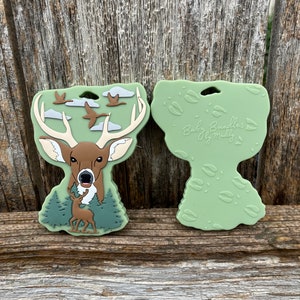 May include: Green silicone teether with a deer and flying geese design. The back side of the teether has a green background with deer footprints. The teether is labeled "Baby Bundles by Maddy".