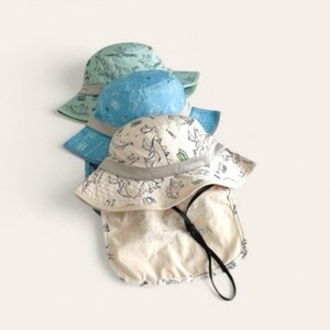 May include: Three sun hats with a dinosaur print. The hats are in shades of blue and green. The top hat is white with a black dinosaur print and a flap that can be pulled down to protect the neck.