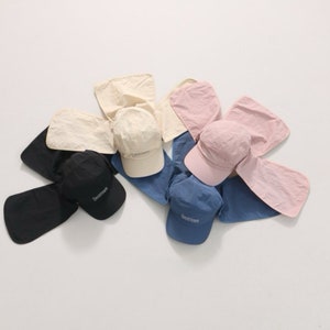 May include: Four sun hats with neck flaps in black, beige, pink, and blue. Each hat has the word "breeze" embroidered on the front.