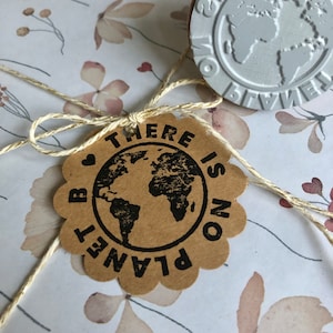 Puede incluir: Un regalo envuelto en papel floral, atado con hilo y una etiqueta marrón. La etiqueta tiene un gráfico de globo negro y las palabras "THERE IS NO PLANET B". Un sello plateado con un globo es visible.