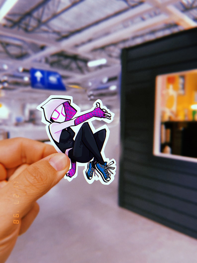 May include: A white and black cartoon sticker of Spider-Gwen, a female superhero, with pink accents, wearing a white hooded suit and blue trainers. She is in a jumping pose with her right arm raised and her left arm extended.