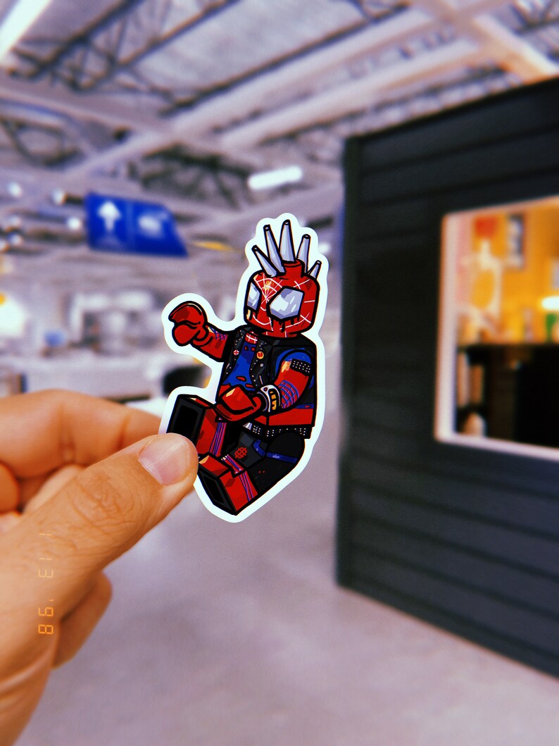May include: A red and blue cartoon sticker of a superhero with spiky hair, wearing a black leather jacket and holding a web shooter. The sticker is on a white background.