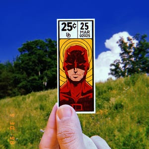 May include: A red and yellow comic book style sticker featuring a character with a red suit and a red devil horn headband. The sticker says "25¢ 25 MAR 02025".