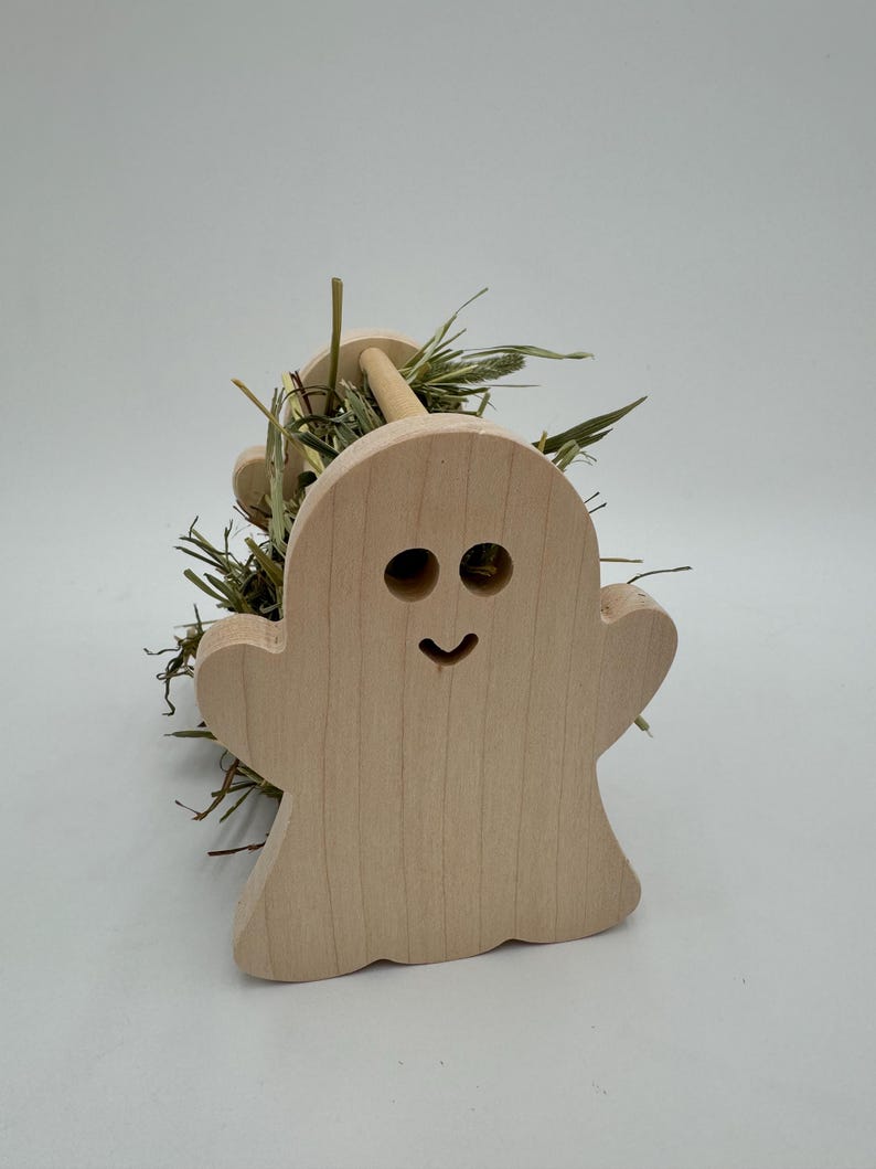Op de afbeelding: Een houten hooiruif in de vorm van een spook voor kleine dieren. De hooiruif is gevuld met gedroogd gras en heeft een glimlachend gezicht.