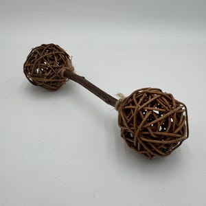 以下が含まれることがあります： 編まれた茶色の小枝で作られた装飾的なダンベル型のオブジェクト。 ダンベルは、茶色の木製のハンドルで接続された2つの球形の端を持っています。 端は紐で包まれています。