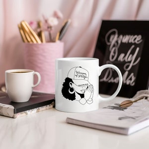 Könnte beinhalten: Weiße Keramiktasse mit einer Schwarz-Weiß-Illustration einer Frau mit Kappe, auf der "Woman of Prayer" und "Proverbs 31:10" steht. Eine kleinere weiße Tasse und ein schwarzer gerahmter Druck sind ebenfalls zu sehen.