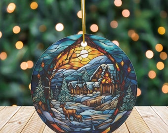 May include: Round Christmas ornament featuring a winter scene with a village, deer, and a sunset. The ornament has a stained glass effect with blue, orange, and brown colors. A gold string is attached for hanging.