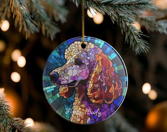 May include: Circular Christmas tree decoration with a stained-glass effect poodle design. The ornament has a gold hanging string and the words "Floofy Doofy". The background is a blurred image of a Christmas tree with fairy lights.