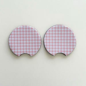 May include: Two pink and white gingham patterned beverage coasters. The coasters are round with a cut-out for a handle.